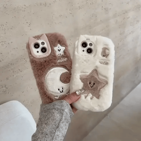 Two fluffy phone cases with cute designs held by a person against a neutral background