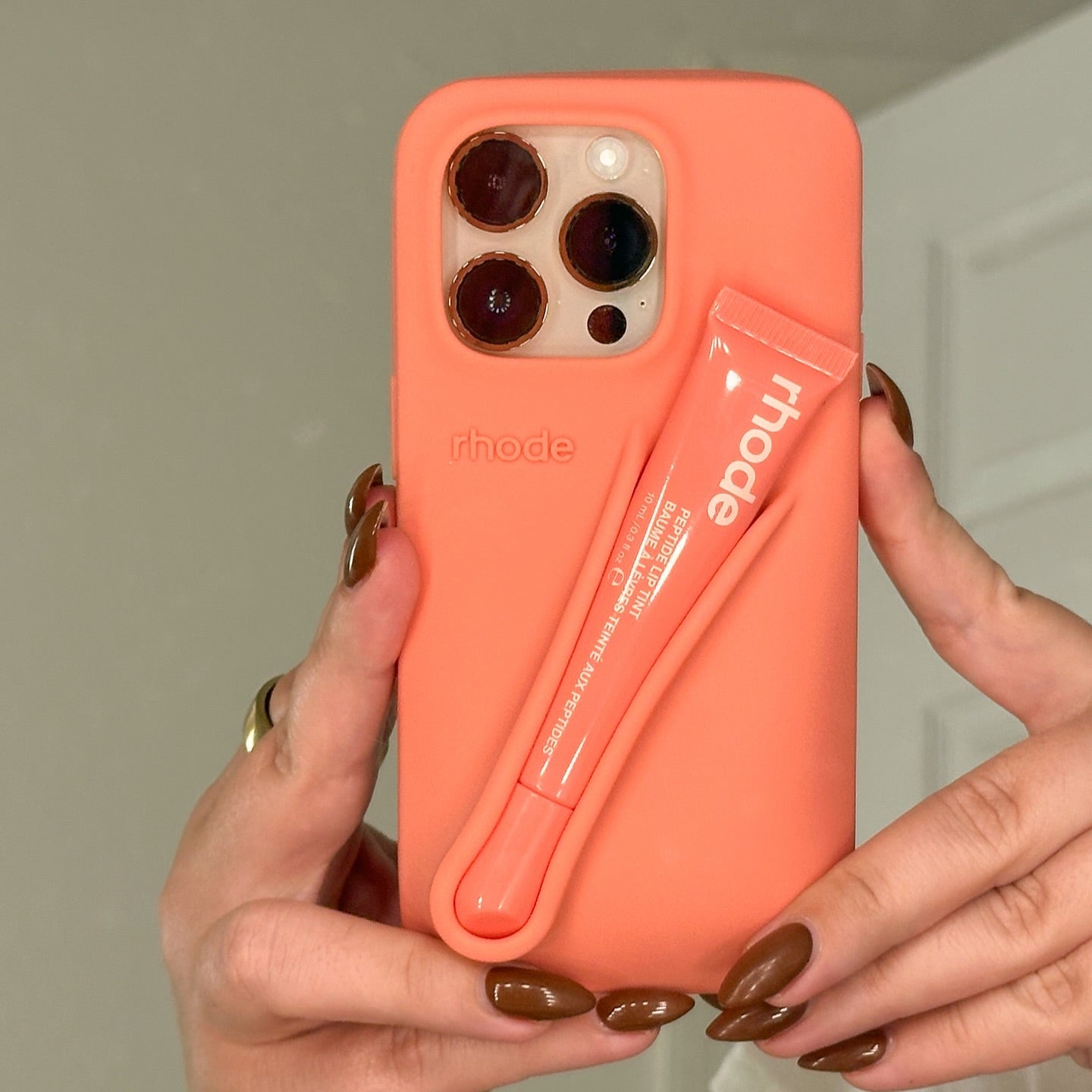 Coral phone case with a built-in lip balm held by hands against a neutral background