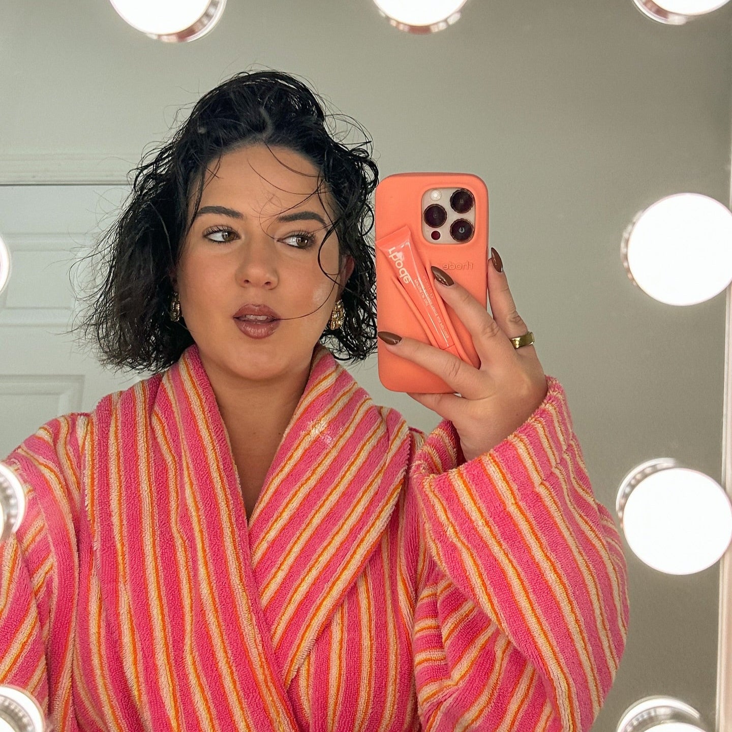 Person wearing a pink and orange striped robe taking a mirror selfie with a phone.