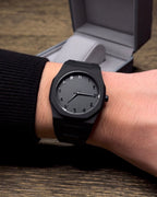 Black wristwatch on a person's wrist with a wooden surface in the background