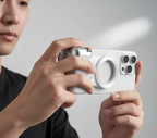 Person holding a white smartphone with a camera module on a plain background