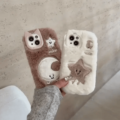 Two fluffy phone cases with cute designs held by a person against a neutral background