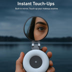 Hand holding a compact mirror with a built-in light, reflecting a person's eye, against a blurred natural background.