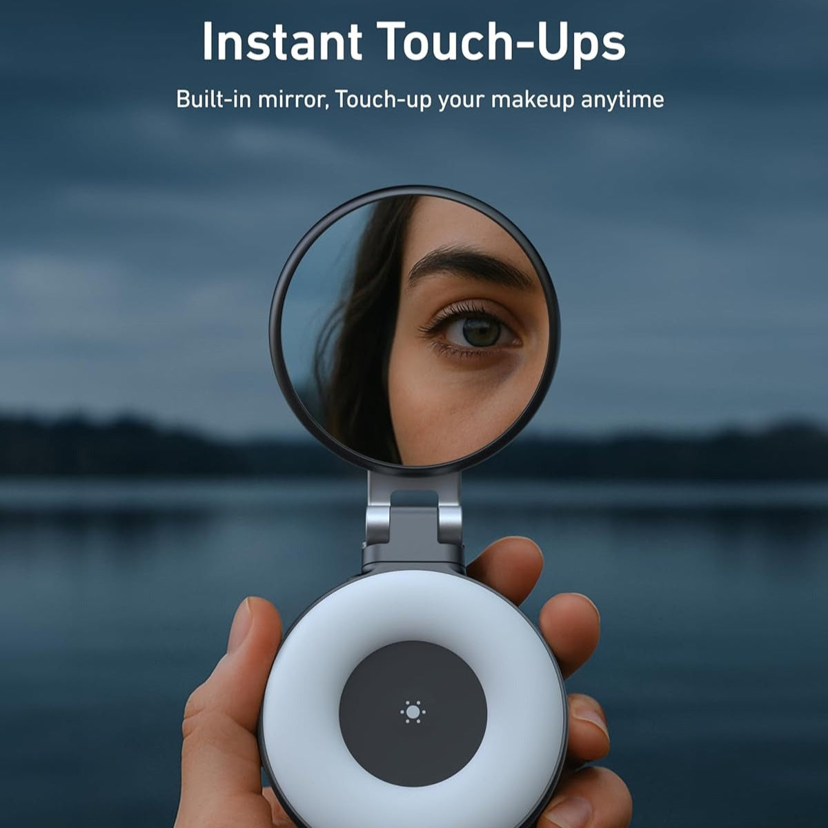 Hand holding a compact mirror with a built-in light, reflecting a person's eye, against a blurred natural background.