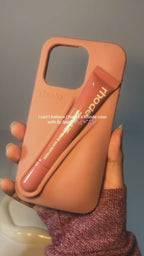 Coral phone case on a white cloth with a peach, next to an orange mesh bag.