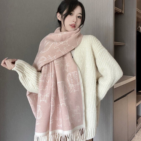 Woman wearing a light pink scarf with white patterns and a cream sweater against a neutral background.
